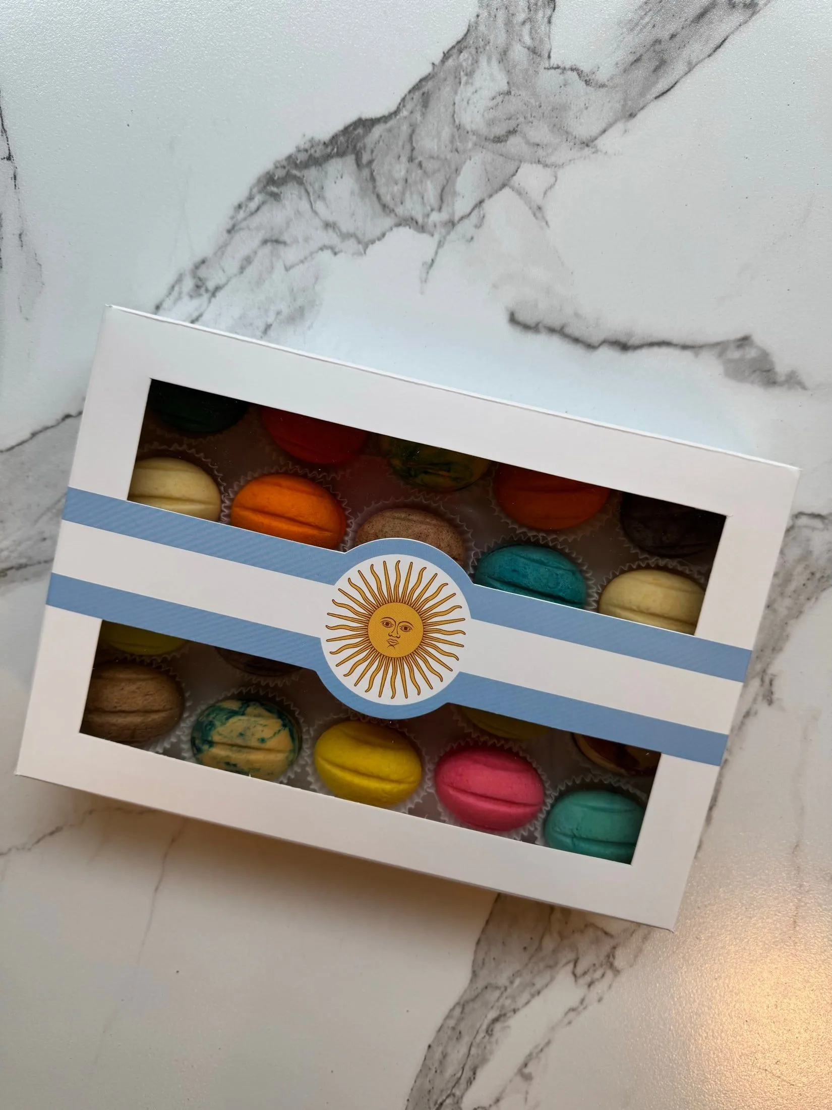 Caja de regalo con ventana llena de oreshki de colores, con una banda con la bandera argentina y el Sol de Mayo